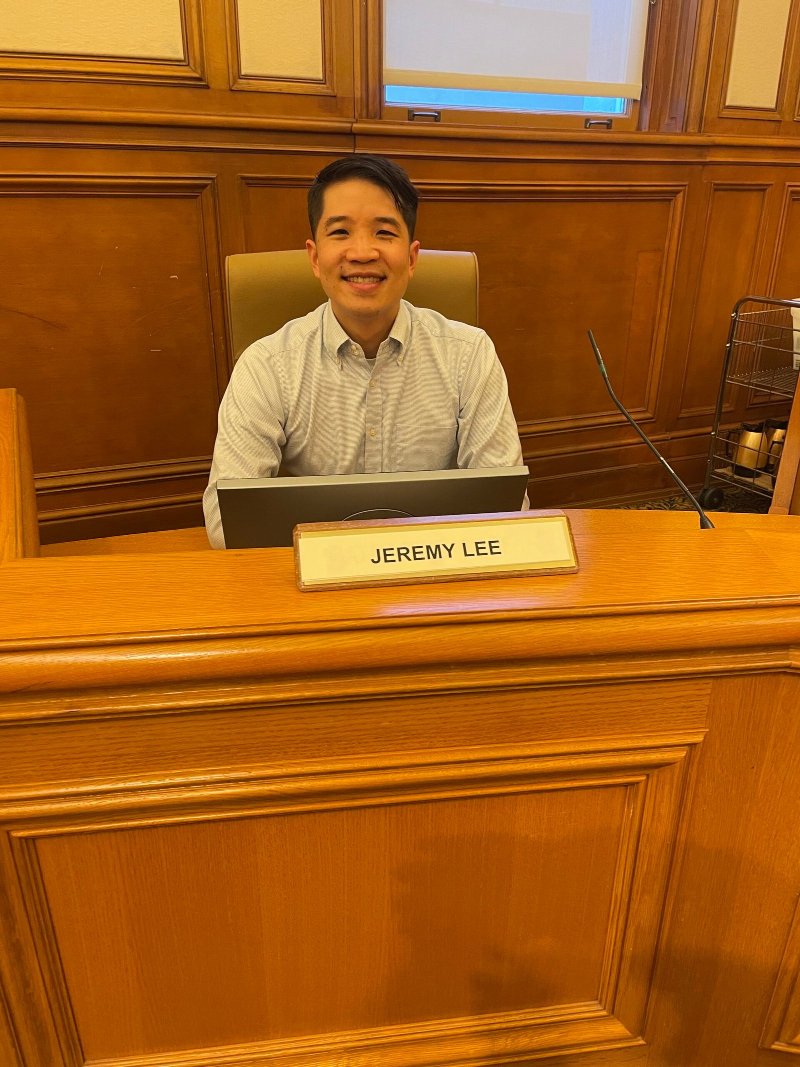 Jeremy Lee seated at a public meeting dais